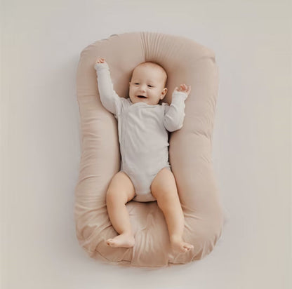 Lächelndes Baby in beigem Babynest, weicher Stoff, gemütlich, sicherer Schlafplatz.
