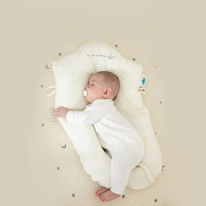 Baby schläft in weißem Babynest auf beigem Hintergrund mit Sternenmuster.