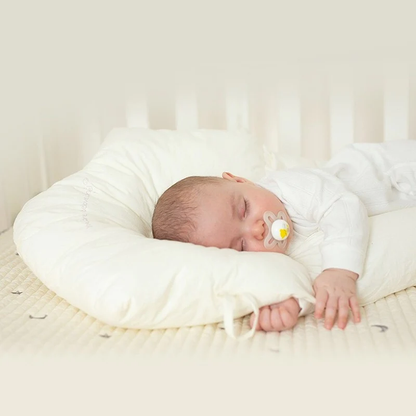 Schlafendes Baby mit Schnuller auf weißem Stillkissen im Kinderbett.