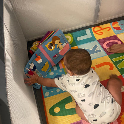Kleinkind spielt mit buntem Stoffbuch auf Alphabet-Spielmatte im Laufstall.