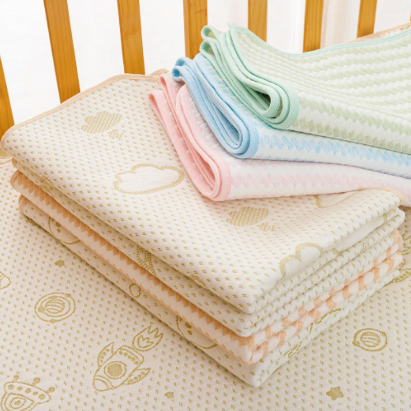 Stapel bunter Babydecken aus Baumwolle mit Mustern auf Holzgitterbett.