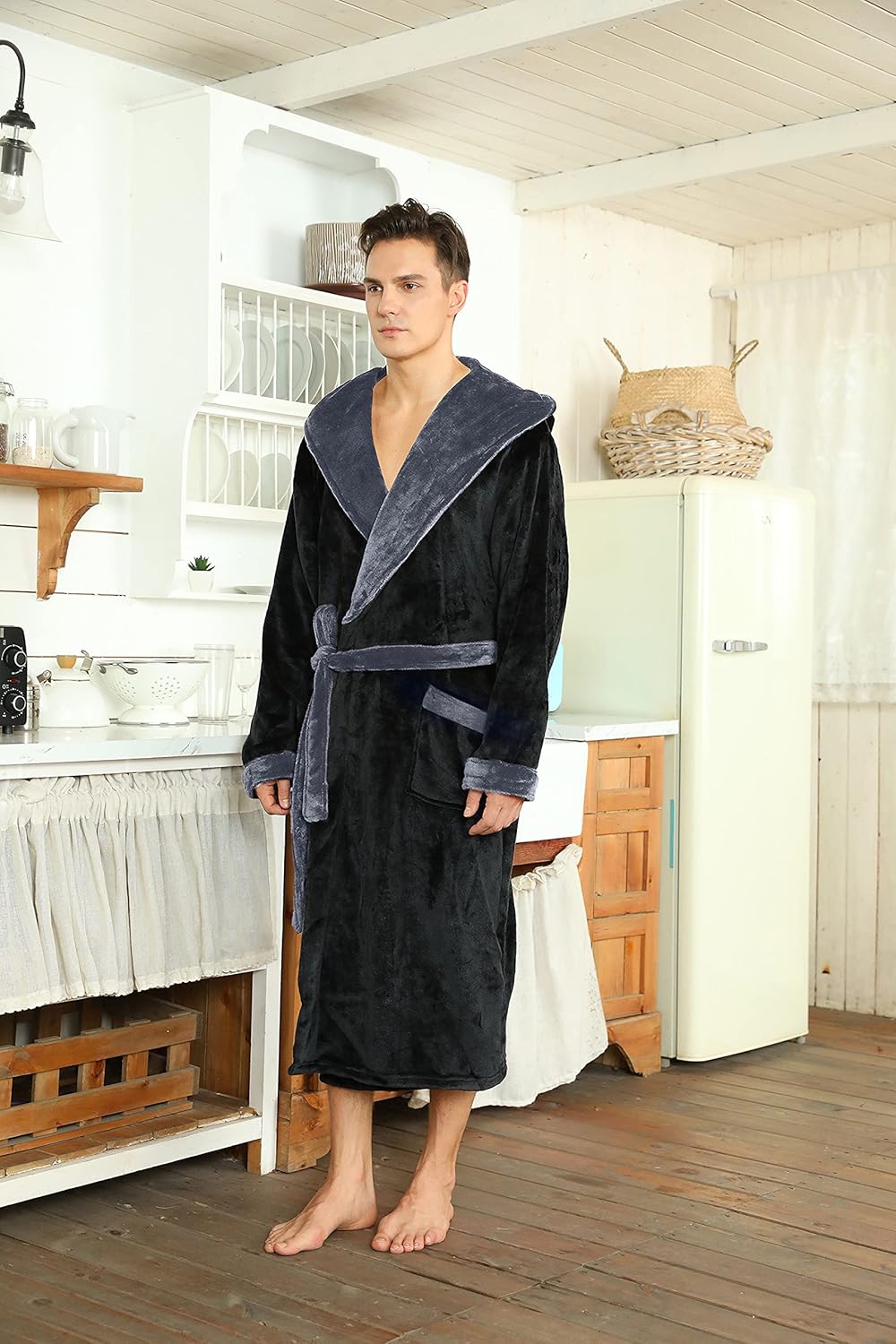 Mann im schwarzen Fleece-Bademantel mit Kapuze in Küche, gemütliche Morgenroutine.