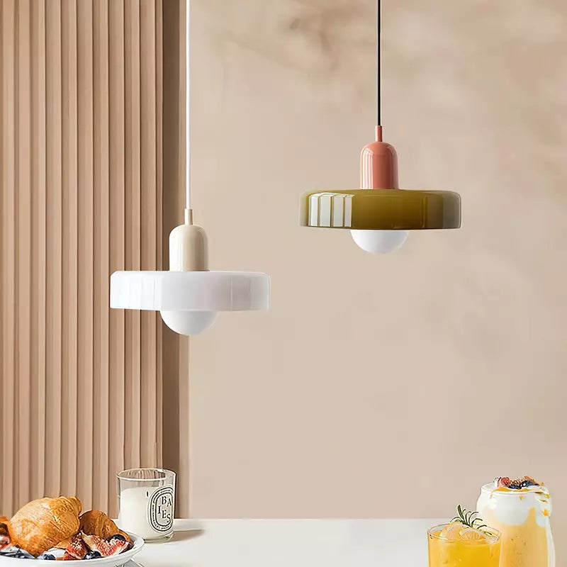 Zwei Bauhaus-Pendelleuchten, weiß und olivgrün, über einem Tisch mit Frühstück.