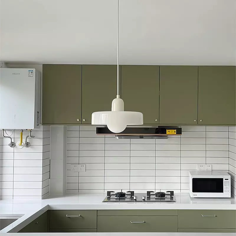 Weiße Pendelleuchte im Bauhaus-Stil über moderner Küche mit grünen Schränken und weißen Fliesen.