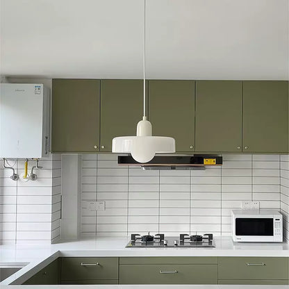 Weiße Pendelleuchte im Bauhaus-Stil über moderner Küche mit grünen Schränken und weißen Fliesen.