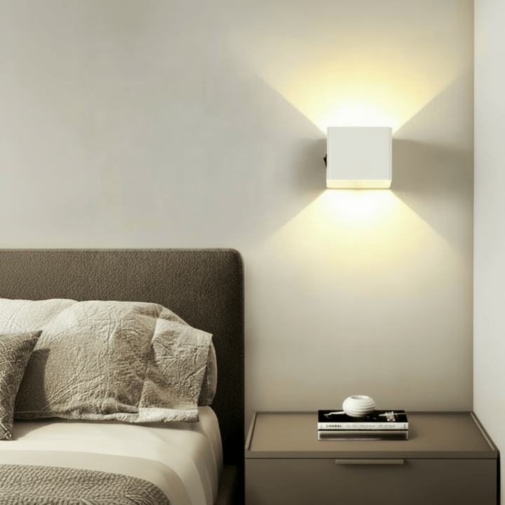 Weiße Wandleuchte leuchtet als Nachttischlampe neben einem Bett mit Kopfteil und wirft Licht fächerförmig nach oben und unten. 3