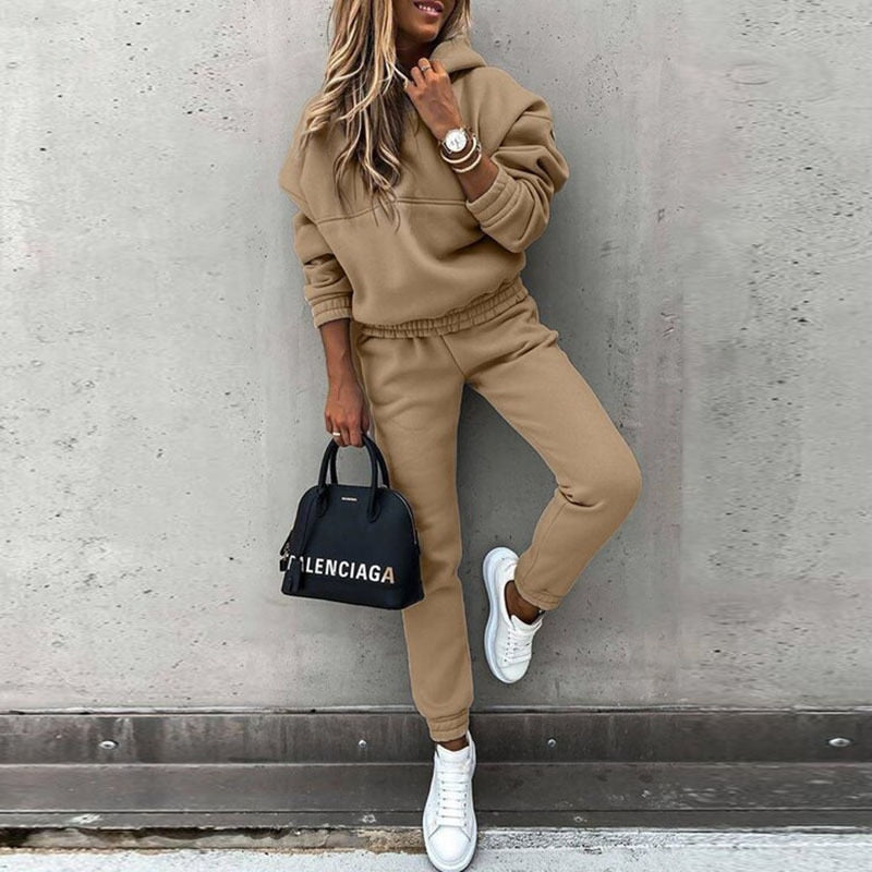 Frau in beigem Jogginganzug, weiße Sneaker, schwarze Handtasche, lässiger Streetstyle-Look.