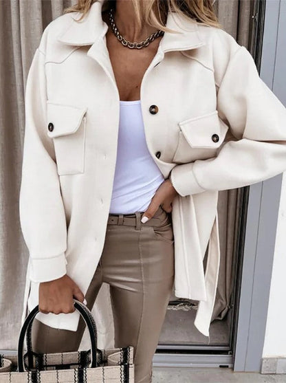Frau in cremefarbener Jacke, weißem Top, beigen Hose, hält gestreifte Tasche, modisch, elegant.