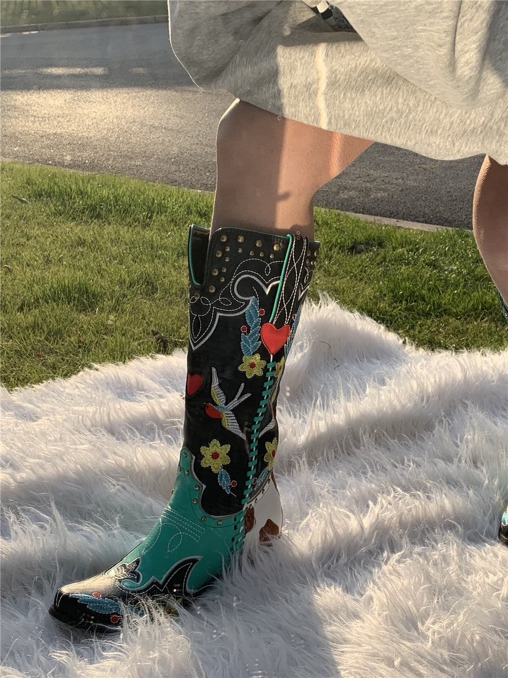 Grüne Cowboystiefel mit Blumenmuster und Nieten auf weißem Teppich im Freien.