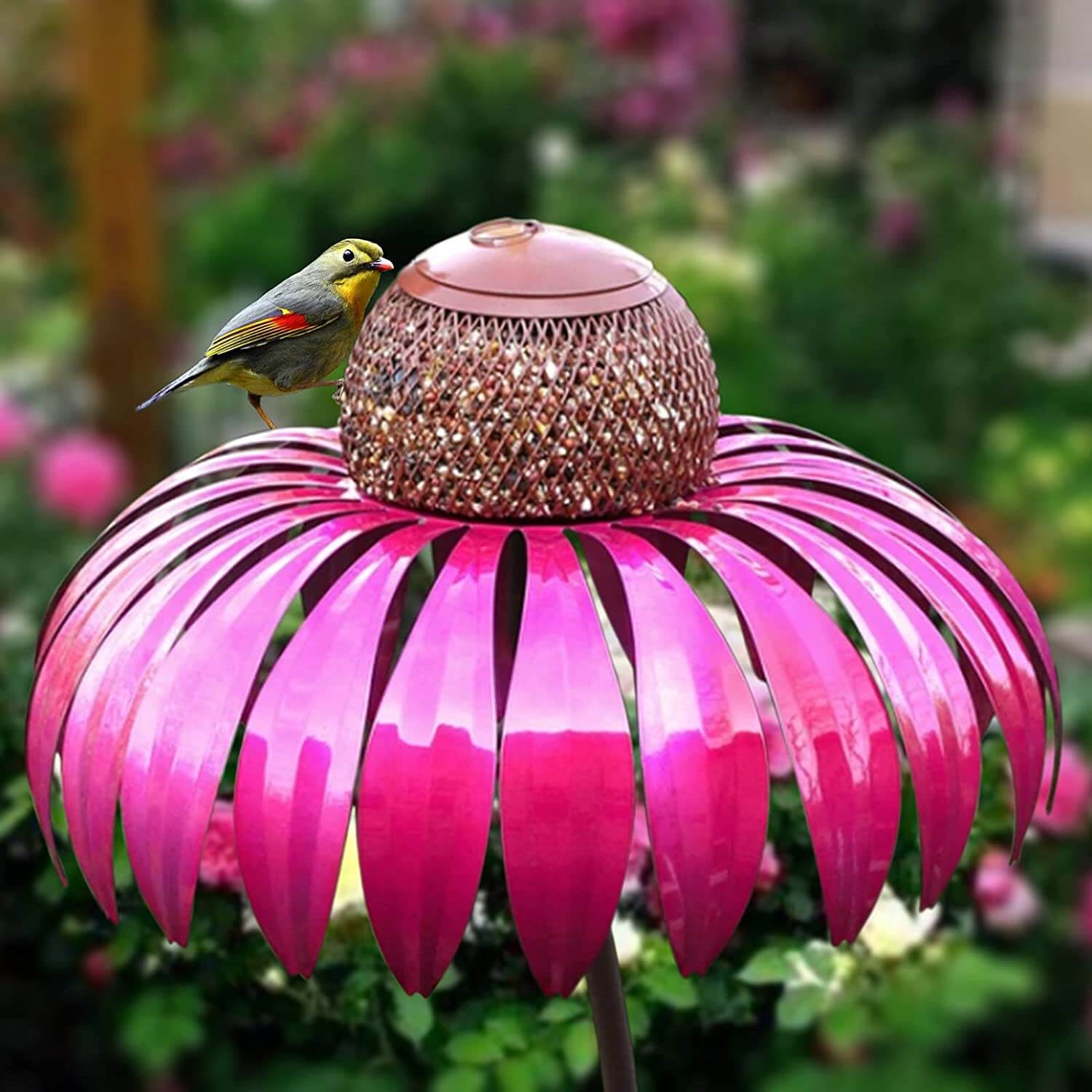 Rosa Metall-Vogelfutterspender mit dekorativem Blütendesign im Garten, Vogel sitzt darauf.