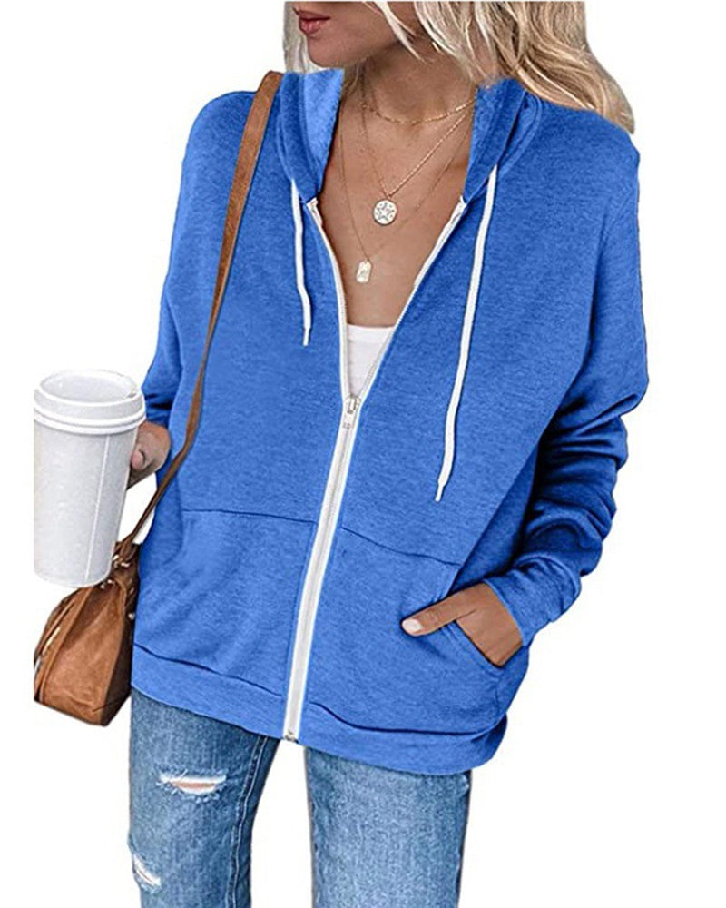 Frau in blauer Kapuzenjacke mit Reißverschluss, Kaffeebecher, Jeans, braune Tasche, lässiger Look.