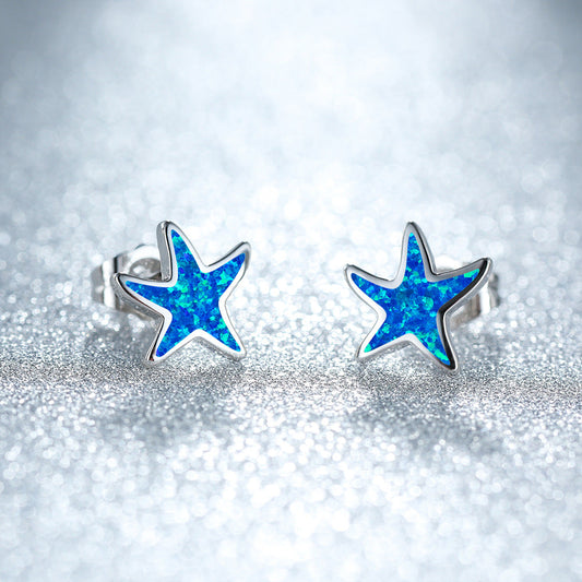 Blaue Stern-Ohrringe aus Silber mit Opal-Effekt auf glitzerndem Hintergrund.