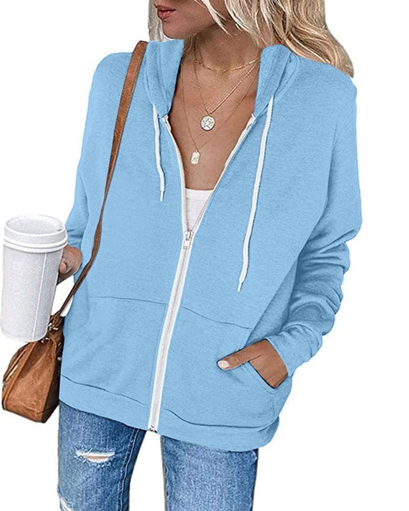 Frau in hellblauer Kapuzenjacke, Jeans, mit Kaffeebecher und brauner Tasche.