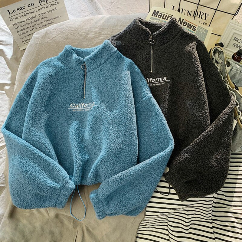 Zwei Fleece-Pullover, blau und grau, mit Reißverschluss und "California"-Aufdruck auf Bett.