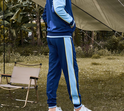 Mann in blauem Trainingsanzug mit gelben Streifen, Outdoor, Campingstuhl, Zelt im Hintergrund.