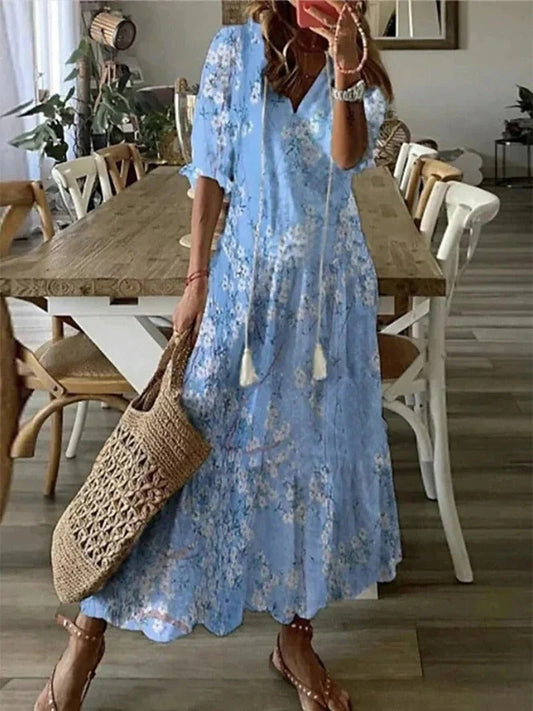Frau in hellblauem Blumenkleid mit Strohtasche, Sommermode, lässiger Stil, Esszimmer im Hintergrund.