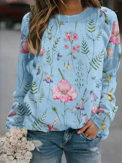 Frau in hellblauem Blumenpullover, Jeans, hält weißen Blumenstrauß.
