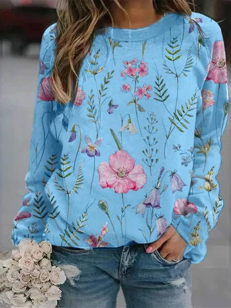 Frau in blauem Blumenpullover, Jeans, hält Rosenstrauß, modische Freizeitkleidung.
