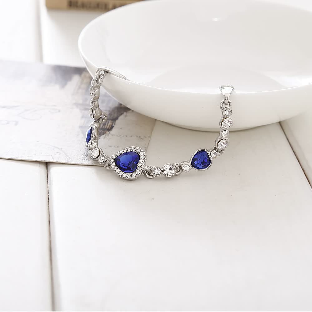 Silbernes Armband mit blauen Herzsteinen und Kristallen auf weißem Hintergrund.