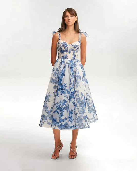 Frau in charmantem blauem Blumenkleid, knielang, mit Spaghettiträgern, elegantes Design.