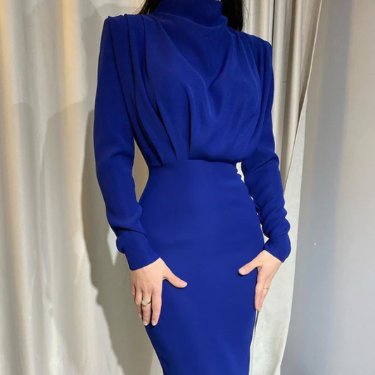 Frau in elegantem, blauem Kleid mit langen Ärmeln vor einem Vorhang.