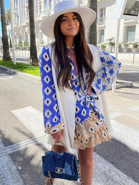 Frau in blau-weißem Kleid mit Hut und Designer-Handtasche auf Straße bei Sonnenschein.