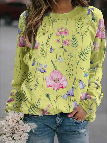 Frau in gelbem Blumenpullover, Jeans, hält weißen Blumenstrauß.