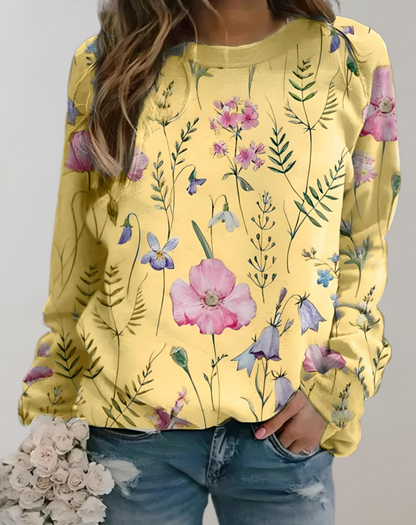 Frau in gelbem Blumenpullover, Jeans, hält weißen Blumenstrauß.