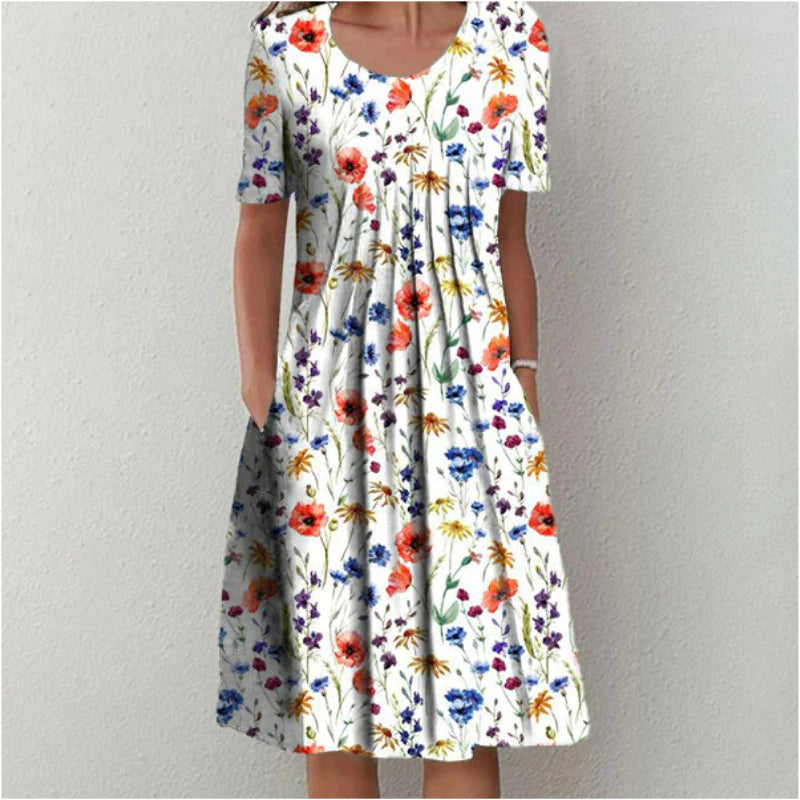 Frau in weißem, geblümtem Sommerkleid mit kurzen Ärmeln und Taschen vor neutralem Hintergrund.