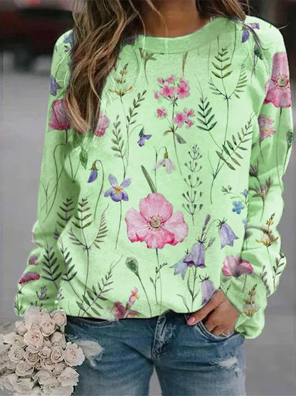 Frau in grünem Blumenpullover, Jeans, hält weißen Blumenstrauß.