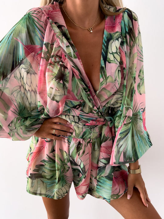 Frau in grün-rosa geblümtem Sommerkleid, V-Ausschnitt, lange Ärmel, tropisches Muster.