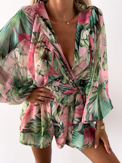 Frau in grün-rosa tropischem Jumpsuit mit Blumenmuster, V-Ausschnitt und langen Ärmeln.