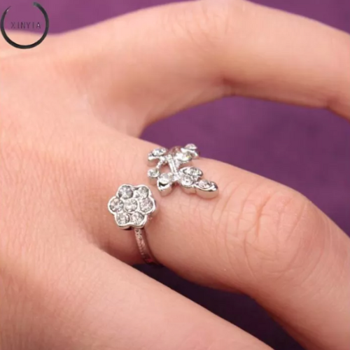 Silberner Blumenring mit Strasssteinen auf Hand, eleganter Schmuck, lila Hintergrund.