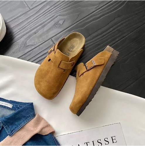 Braune Wildleder-Schlupfclogs auf Holzboden, modisch, bequem, ideal für Herbstmode.