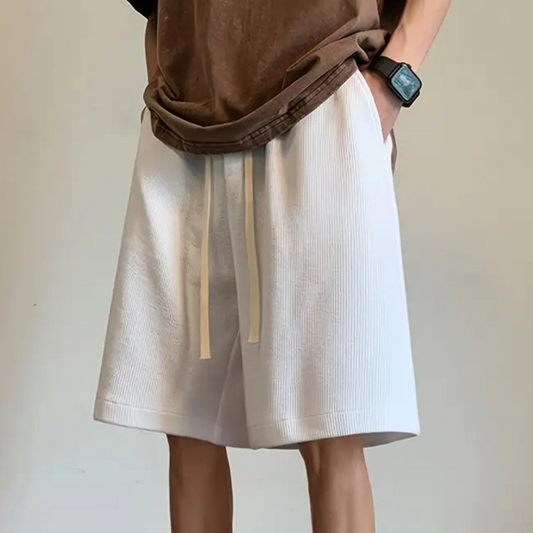Person in weißen Shorts mit Kordelzug, braunes T-Shirt, Armbanduhr, lässiger Stil.