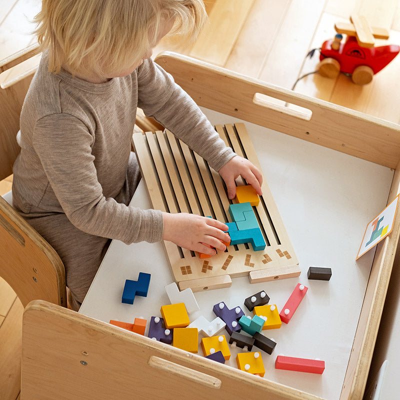 Kind sitzt von oben gesehen an einem Holztisch und legt Steine auf das Brett, auf der Tischfläche liegen weitere bunte Teile. 8