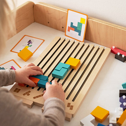 Kinderhände schieben bunte Holzsteine in die Schlitze des Bretts, im Hintergrund stehen Vorlagenkarten mit Mustern. 3