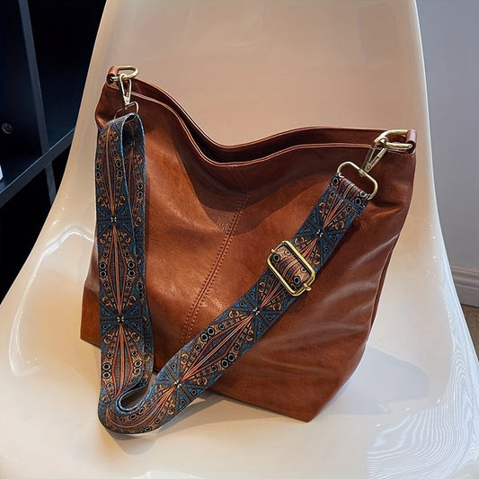 Braune Ledertasche mit verziertem Schultergurt auf weißem Stuhl, modisch und elegant.