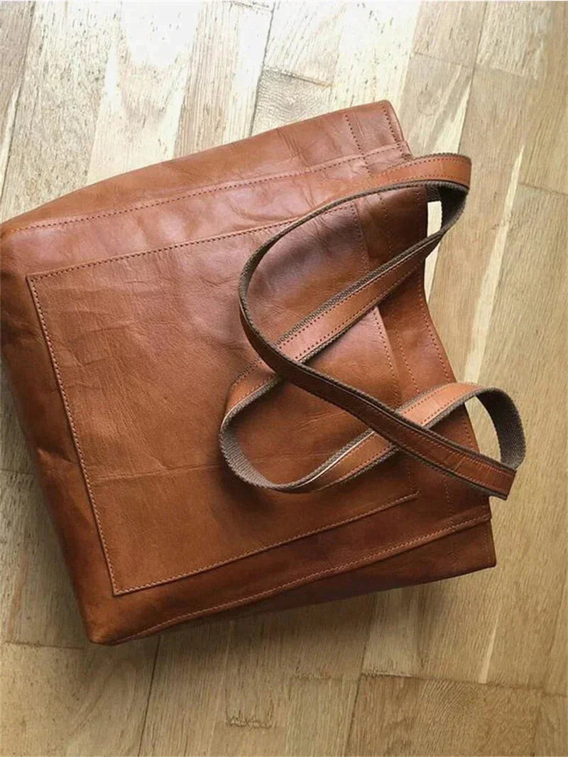 Braune Ledertasche auf Holzboden, langlebig, modisch, Einkaufstasche, Damenaccessoire.