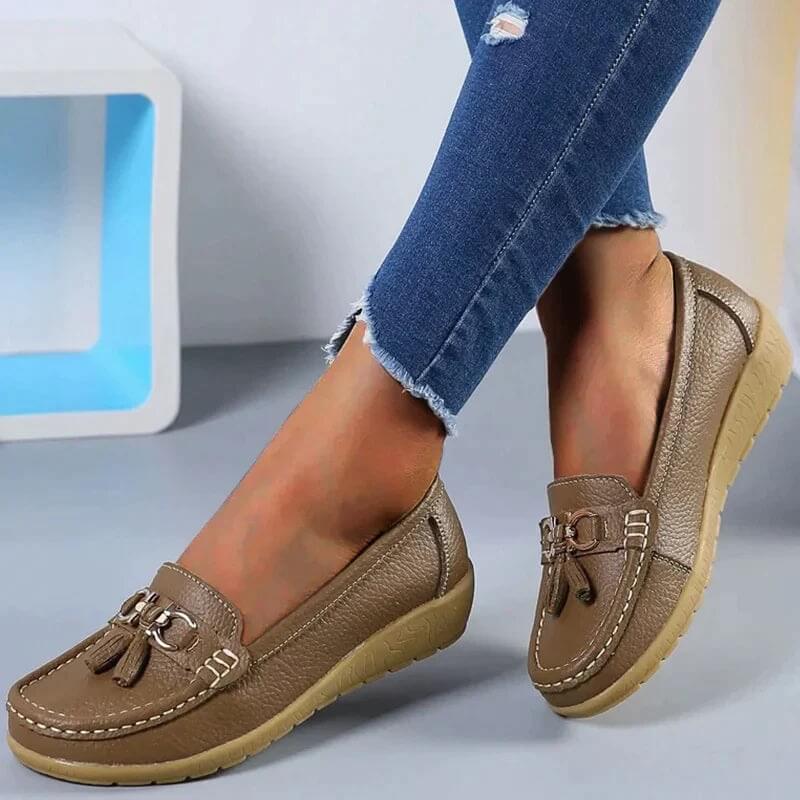 Braune Damen-Mokassins aus Leder mit Quasten, bequeme Freizeitschuhe, Jeanshintergrund.