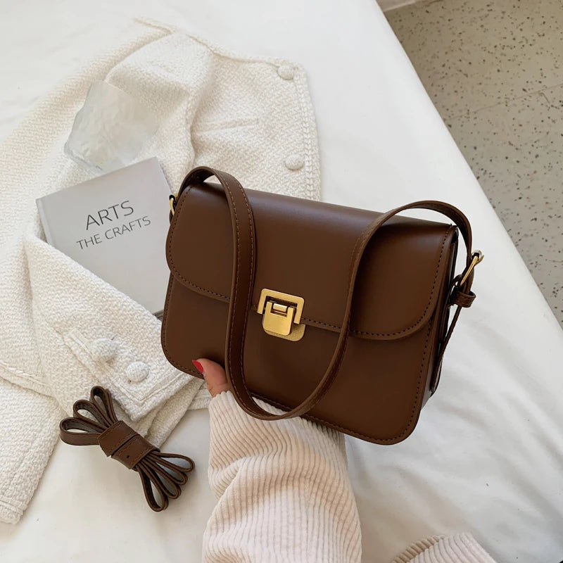 Braune Lederhandtasche mit goldener Schnalle auf weißem Stoff, modisch und elegant.