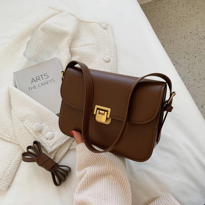 Braune Lederhandtasche mit goldener Schnalle auf weißem Stoff, modisch und elegant.