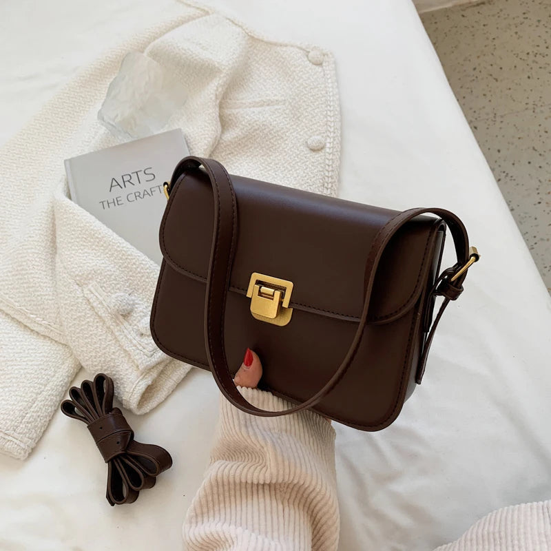 Dunkelbraune Ledertasche mit goldener Schnalle auf weißem Bett, modisch, elegant, Damenaccessoire.