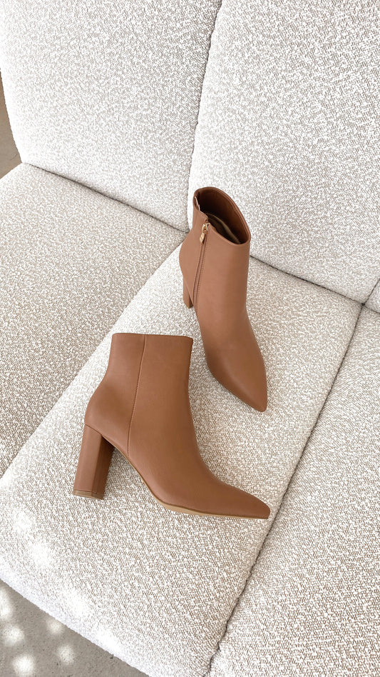 Braune Damen-Stiefeletten aus Leder mit Blockabsatz auf beigem Sofa, modisch und elegant.