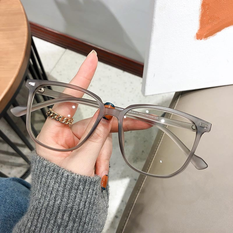 Graue, rechteckige Brille aus Kunststoff, modisch, unisex, Nahaufnahme, Hand hält Brille.