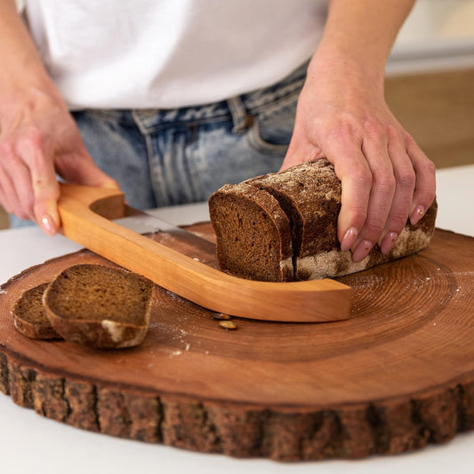 Person schneidet Roggenbrot auf Holzbrett mit Brotmesser, Nahaufnahme, Küche, Backen.