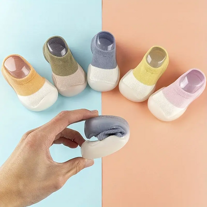 Fünf Paar bunte Babysocken mit rutschfester Sohle auf zweifarbigem Hintergrund.