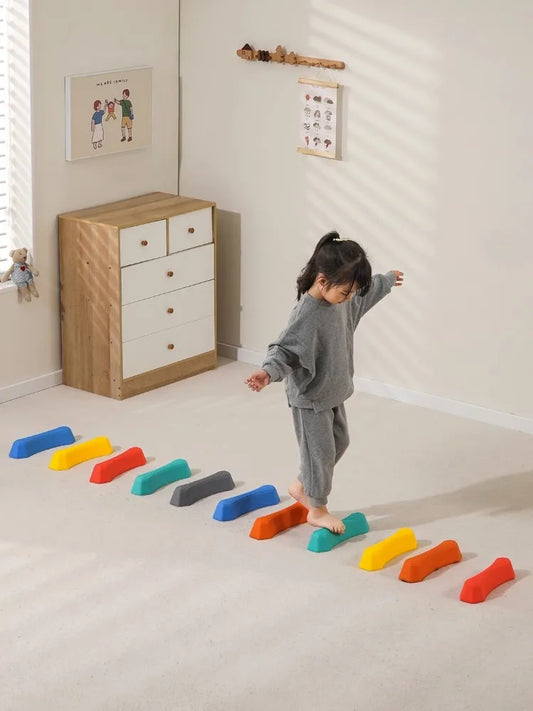 Kind spielt auf bunten Balanciersteinen im Kinderzimmer, grauer Anzug, Holzmöbel im Hintergrund.