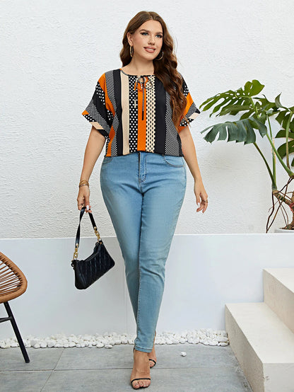 Frau in gestreifter Bluse und blauer Jeans, hält schwarze Handtasche, steht vor weißer Wand.