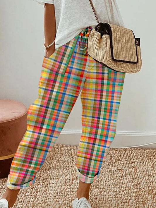 Frau in bunter Karohose, weißem T-Shirt und Strohtasche, modisch, lässig, trendig.